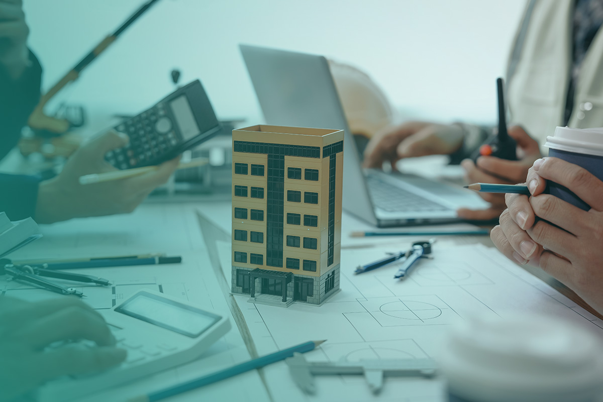 “A team reviewing building plans and calculations beside a scale model of a property, representing compliance work for Heat Network Regulations.”