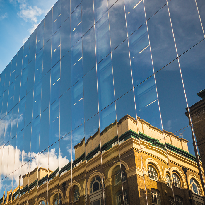 Glass-fronted modern building reflecting an older property — highlighting the MEES risks for landlords with mixed portfolios.