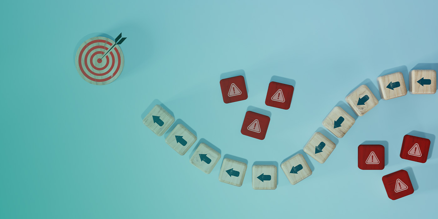 Wooden blocks with arrows navigating around red warning symbols towards a target, symbolising risk, control, and opportunity in developing a flexible energy procurement strategy 2025.