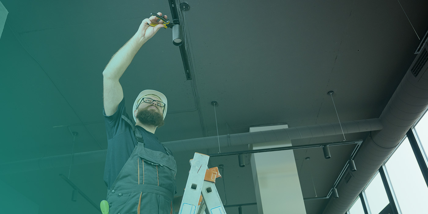 “Engineer on a ladder adjusting ceiling lighting, representing operational planning issues that often lead to Energy Procurement Mistakes.”