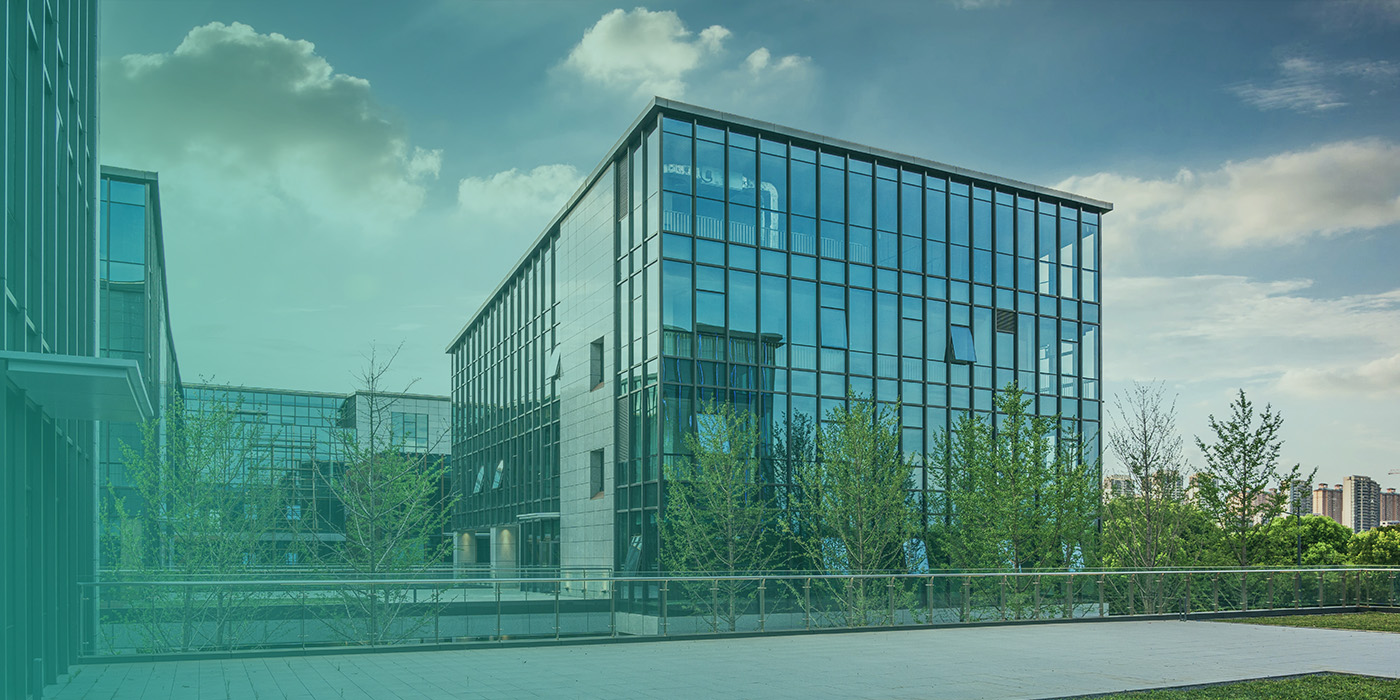 Modern glass fronted office building surrounded by greenery, illustrating how BMS Optimisation improves comfort, efficiency, and operational performance in commercial spaces.