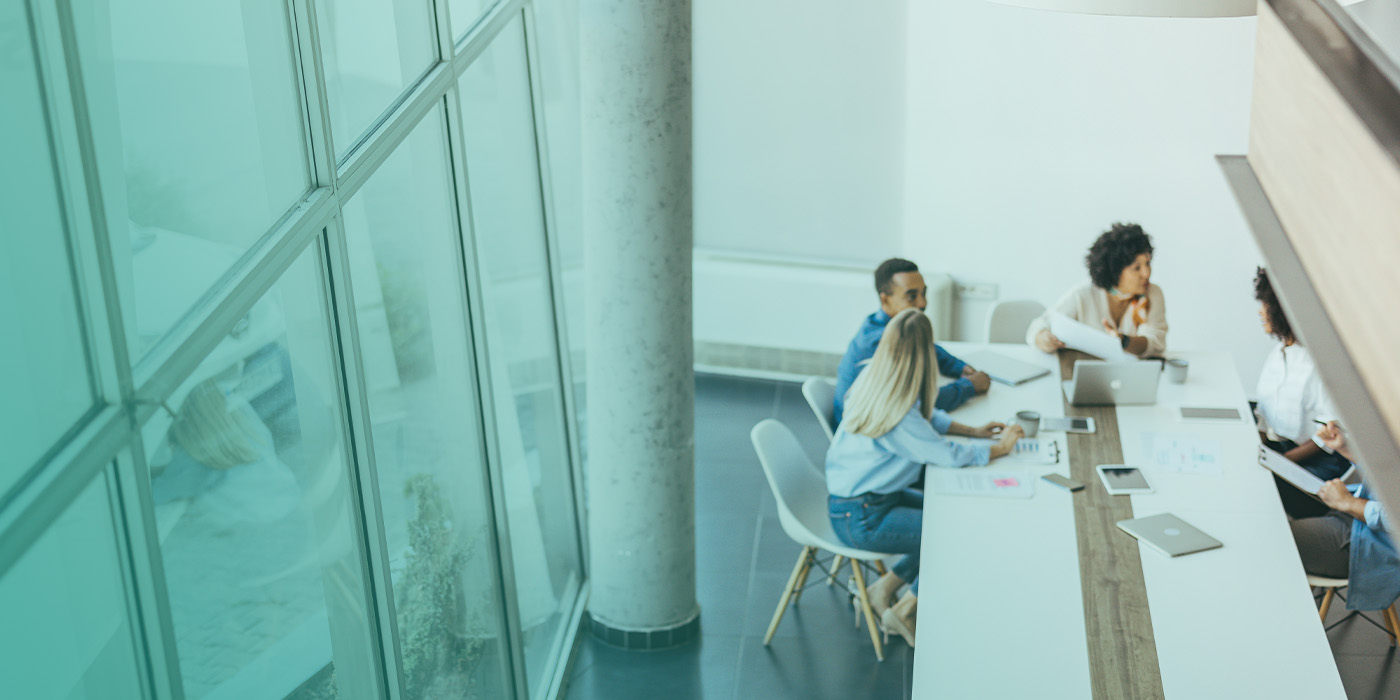 A team of people sitting around a meeting table in a modern office discussing building performance actions as part of a BMS Optimisation Checklist.